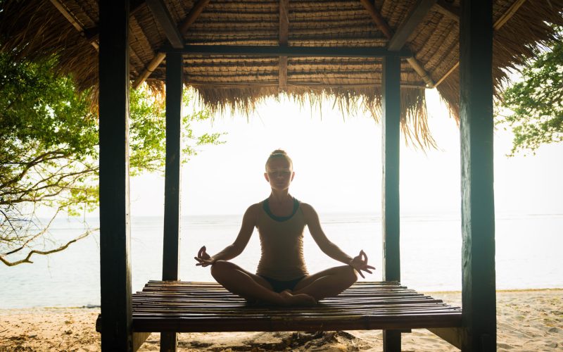 Young woman meditating in lotus pose at the ocean shore